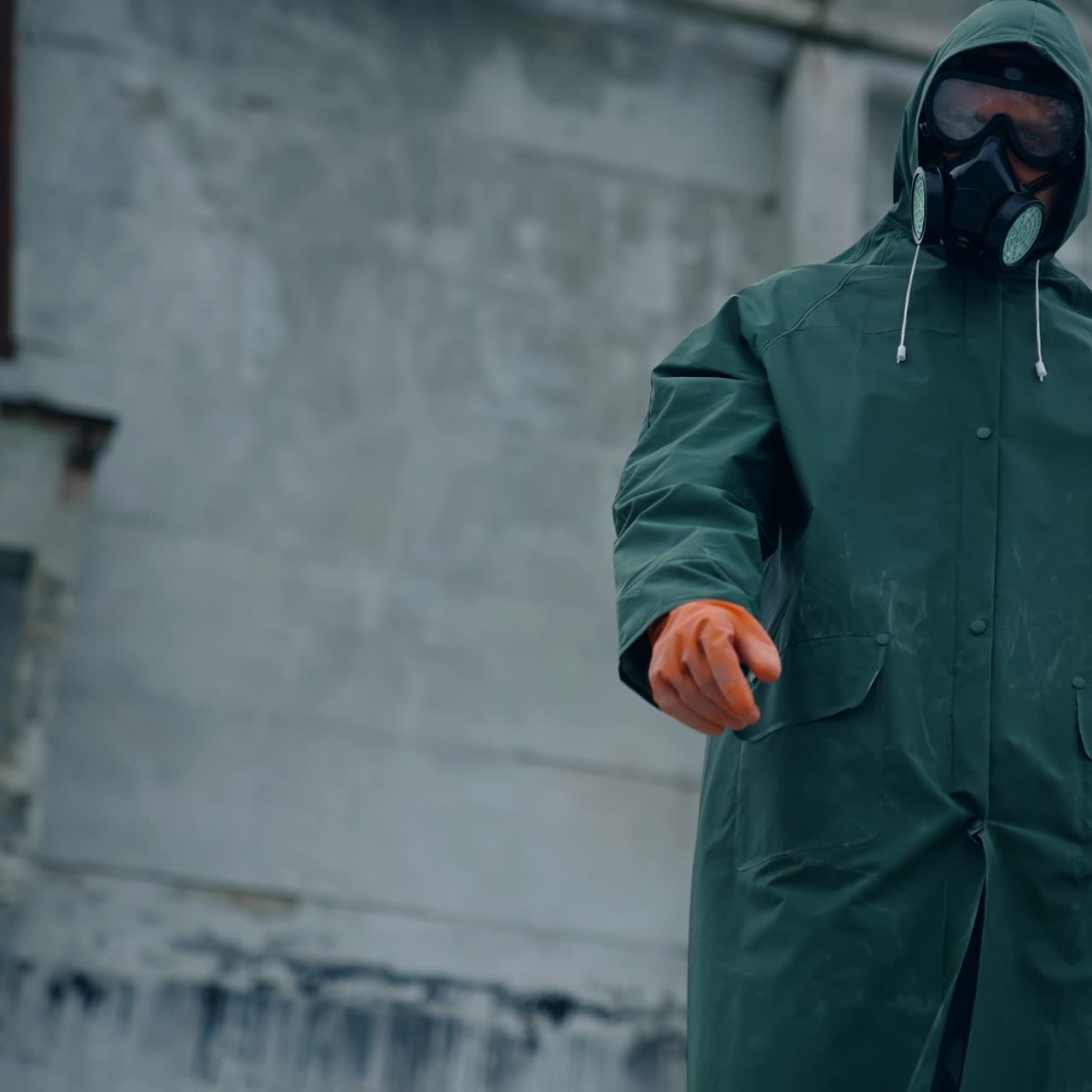 Human in protective costume and mask in infected place. Survivor man in a mask and a chemical protection suit showing on the camera with a finger