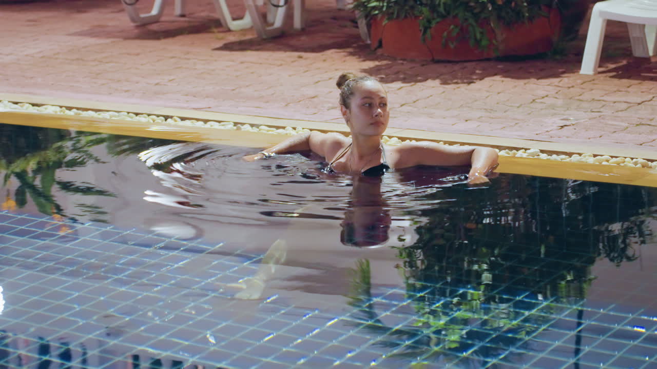 Junge Frau tollt sich am sonnigen Pool. Frau spielt in einem Inselpool mit fröhlichen Spritzern und Lächeln. Frau hat Spaß in einem tropischen Pool, umgeben von Sonnenlicht und fröhlicher Atmosphäre
