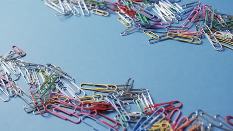 close up of scattered colourful paper clips with copy space on blue background, in slow motion