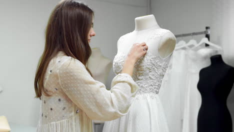 Portrait-of-a-girl-creating-a-wedding-dress-by-exclusive-order-sewing-fabrics-and-rhinestones-on-a-dress-dressed-in-a-mannequin.-production-of-wedding-dresses.-Little-business