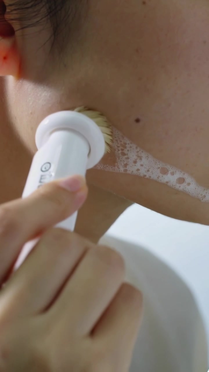 Vertical video: Positioning woman using white electric brush along jawline in bathroom