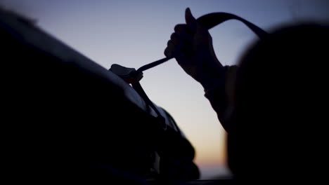 person adjusting car strap at sunset