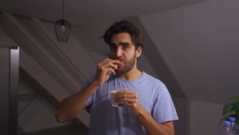 hombre mojando una galleta con trocitos de chocolate en un vaso de leche y comiéndola mientras hace muecas
