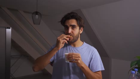 man dipping a chocolate chip cookie in a glass of milk and eating it while making funny faces