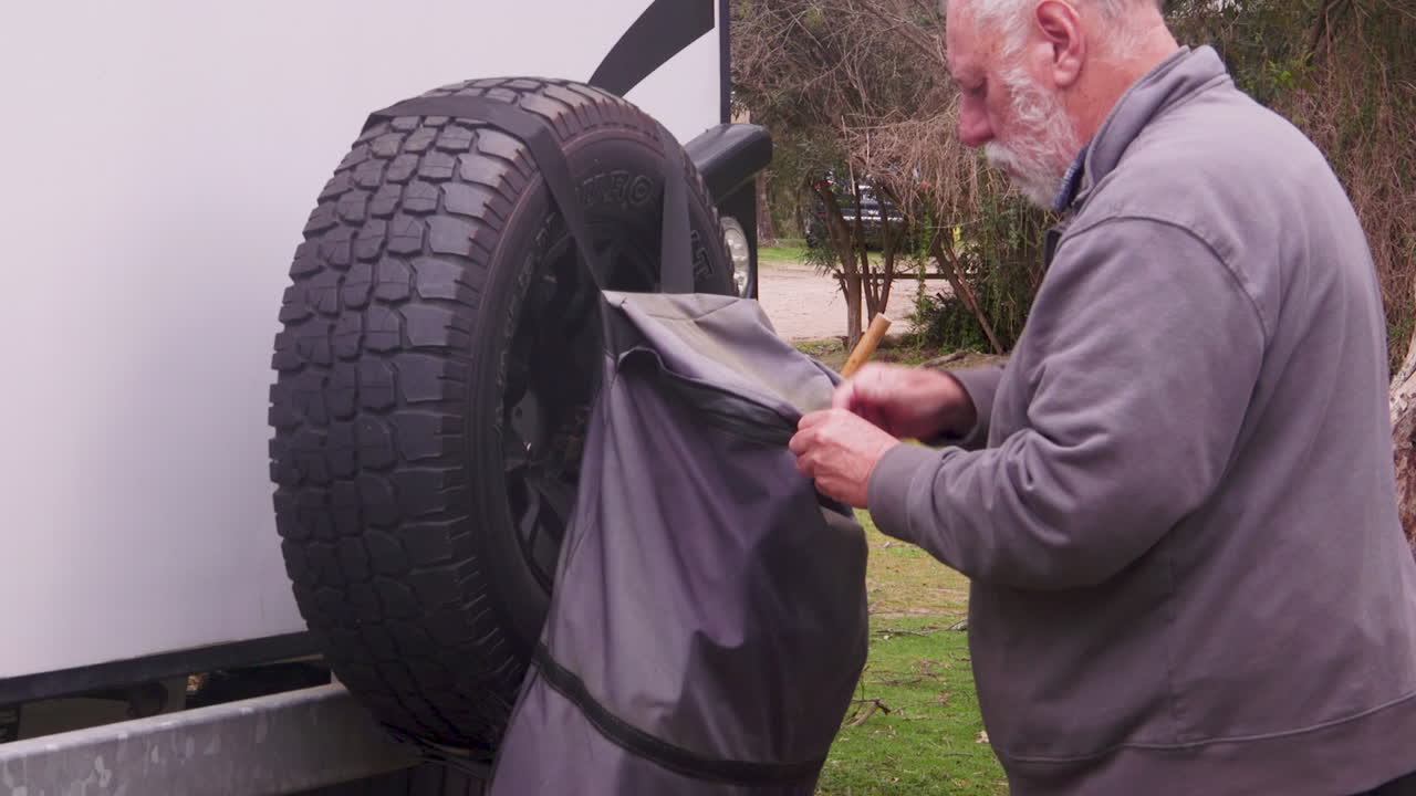 A camper places rubbish into a convenient camping bin attached to an RV caravan. The activity takes place in a serene outdoor setting, promoting responsible waste management while enjoying nature