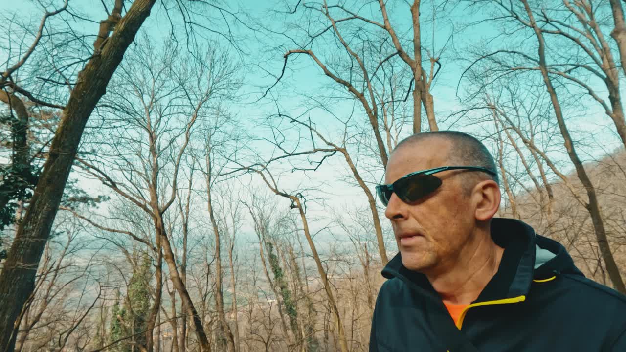 Modern mature man using headphones to listen to an educational podcast or music while walking in nature. Intersection of technology and wellness in senior years
