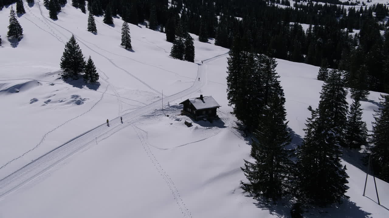 Inverno in montagna. Ripresa aerea che si allontana da uno chalet. Alcune persone sciano
