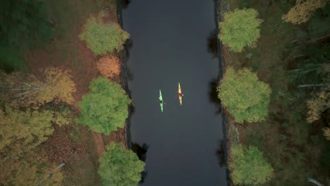 two adventurers kayaking through calm forest river in fall, bird’s eye view