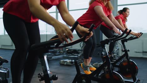 Group-of-smiling-friends-women-class-exercising,-training,-spin-on-stationary-bike-at-modern-gym