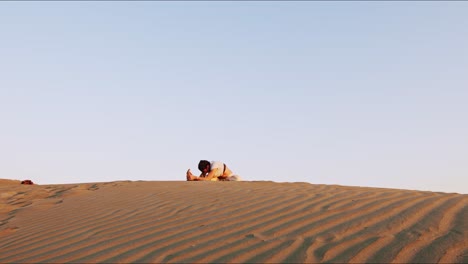 Young-brunette-yoga-instructor-on-a-sand-hill-performing-a-morning-yoga-routine-and-stretching-during-golden-hour