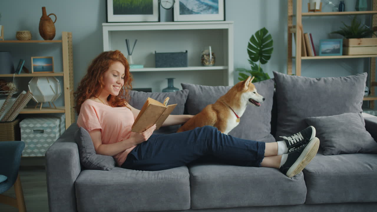 Woman Reading a Book with a Dog on the Couch