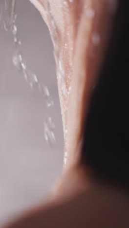 woman neck with water drops in shower unit closeup. graceful lady relaxes standing in warm sprays in home bathroom. hygienic routine for body