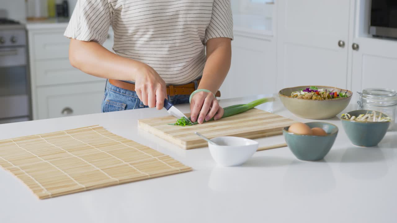 Donna afroamericana che affetta cipollotti con un coltello su un tagliere sull'isola della cucina, preparando il pasto.