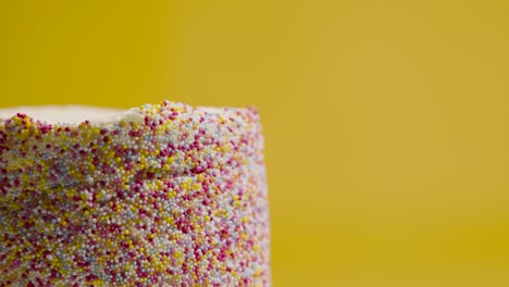 close up studio shot of revolving birthday cake covered with hundreds and thousands decorations 3