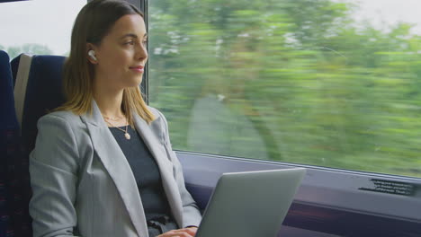 businesswoman with wireless earbuds commuting to work on train working on laptop