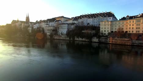 Drohne-über-Dem-Rhein-In-Basel-Dreht-Sich-Um,-Enthüllt-Den-Sonnenaufgang-Und-Steigt-Auf,-Um-Die-Stadt-Zu-Betrachten