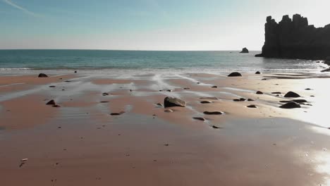 toma aérea sobre una playa de arena con rocas, avanzando hacia el mar