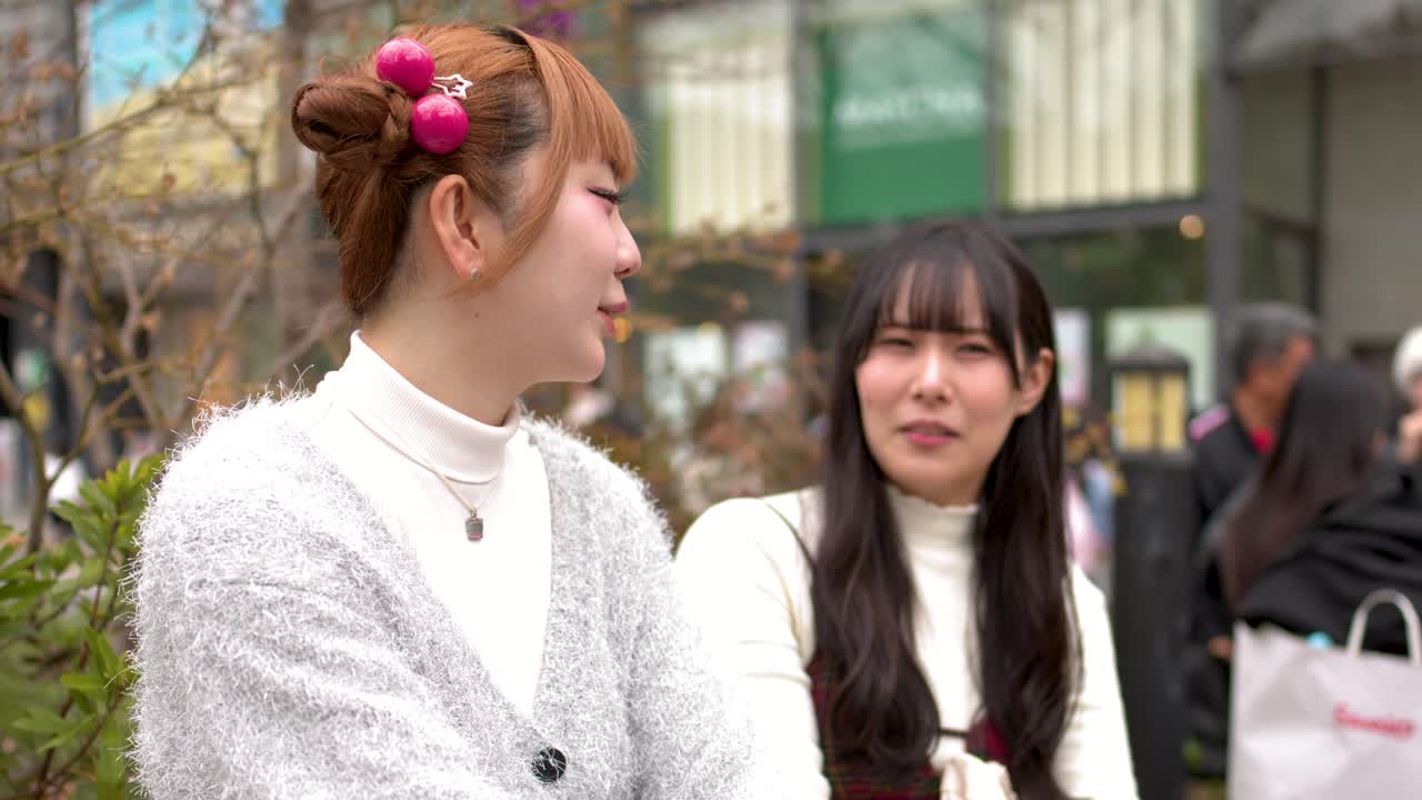 東京の屋外で、自然光の中で談笑する2人のスタイリッシュな若い女性。