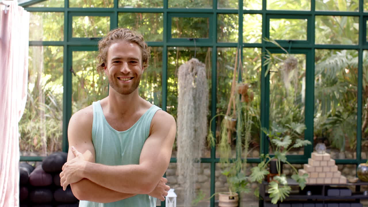 Smiling man in tank top standing with arms crossed in glass house garden, copy space