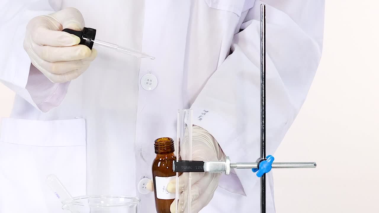Un ricercatore che indossa guanti bianchi e un camice da laboratorio maneggia un contagocce e una bottiglia di prodotti chimici