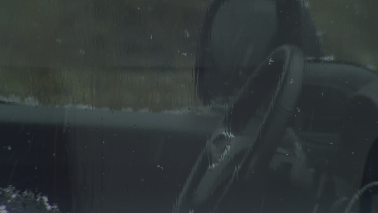 Looking into an empty car, steering wheel visible. Melted snow running down the side window, more snow falling. Static close up shot.