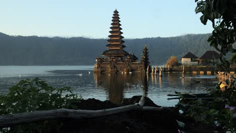 ascending shot of a magnificent hindu temple located in the water of pura segara ulun danu at volcano lake batur during golden hour and calm waters reflecting off the lake