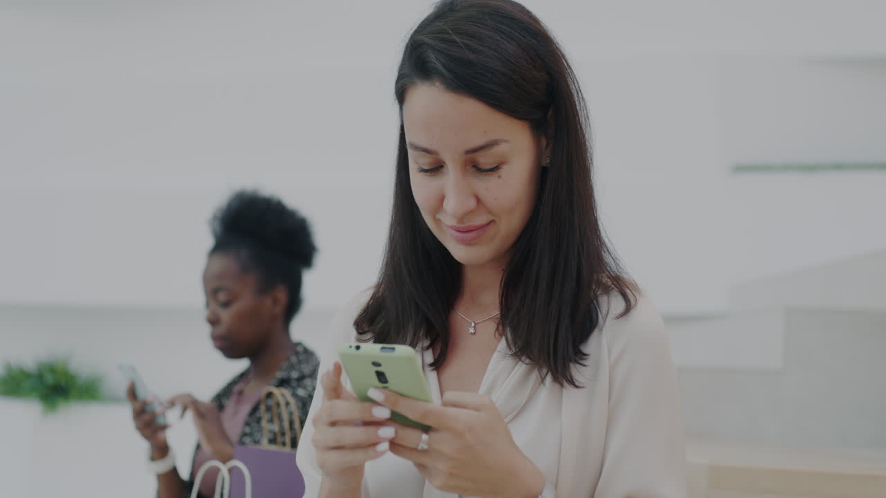 Two women using phones in a shopping mall