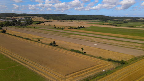 Die-Drohne-Zieht-Sich-Zurück-Und-Zeigt-Vögel,-Die-über-Herrliche-Landschaften-Mit-Goldenen-Und-Grünen-Feldern-Und-Wiesen-Mit-Flauschigen-Wolken-Fliegen