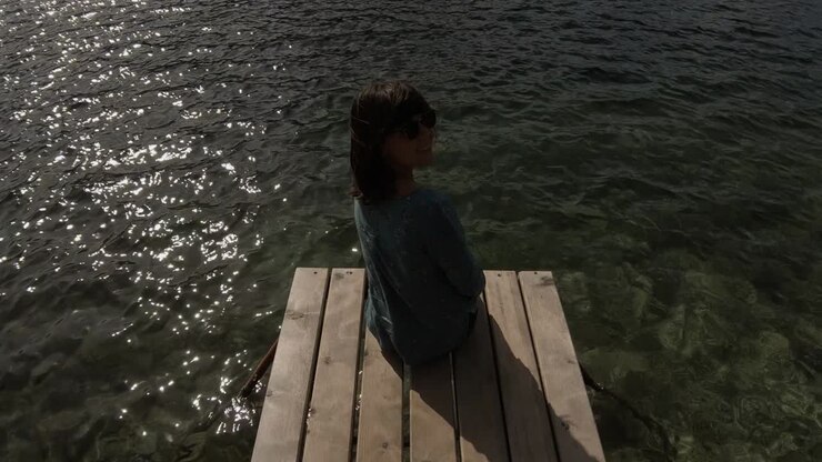 A gorgeous brunette sitting at the end of a pond and looking at the waters