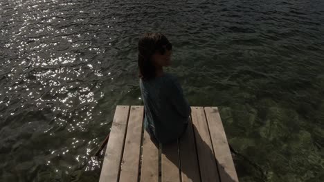 A-gorgeous-brunette-sitting-at-the-end-of-a-pond-and-looking-at-the-waters