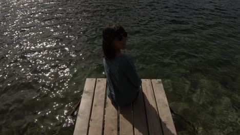 a gorgeous brunette sitting at the end of a pond and looking at the waters