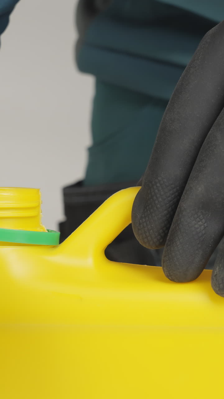 Person Handling a Yellow Chemical Container with Protective Gloves