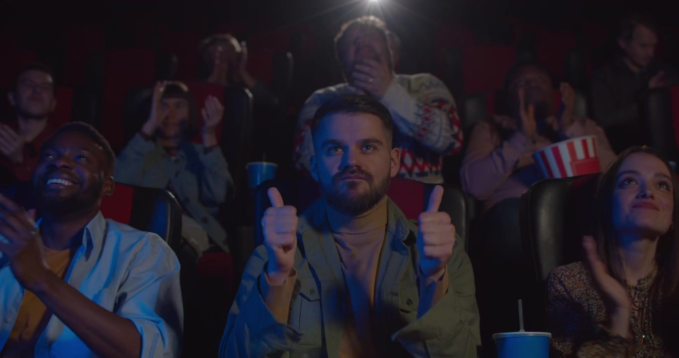 Gruppo eterogeneo di amici che applaudono mentre guardano un film al cinema