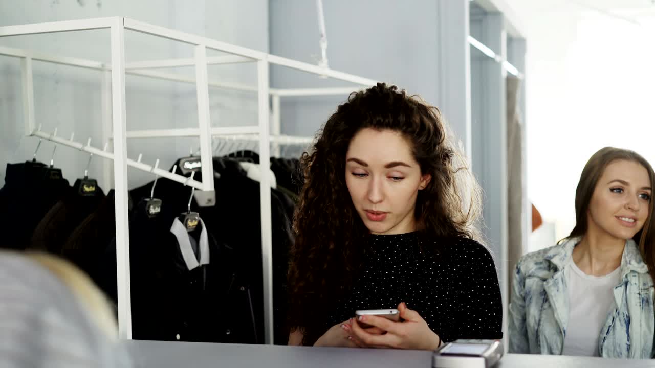 fotografía en primer plano de clientes femeninas pagando por ropa en el mostrador del cajero en una boutique de ropa. mujer joven está haciendo el pago con teléfono inteligente, tomando la bolsa con las compras y saliendo