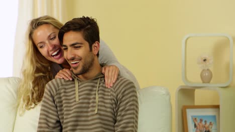 Blonde-girl-whispering-a-secret-to-her-boyfriend-on-the-couch