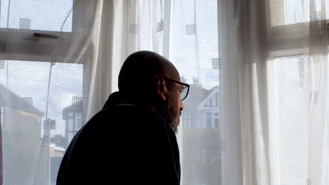 Silhouette-Of-Bald-Male-Talking-On-Phone-Beside-Window-Curtains-Moving-Side-To-Side-Evoking-Nosey-Neighbour,-Observational-Concept