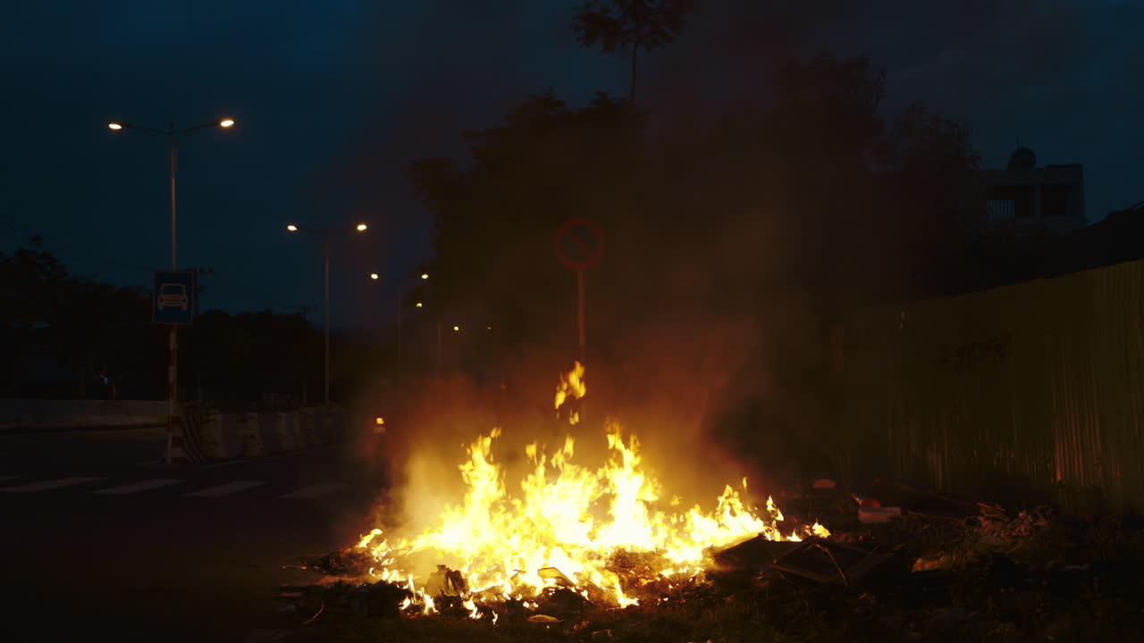 Large bonfire burning on the side of an urban road at night