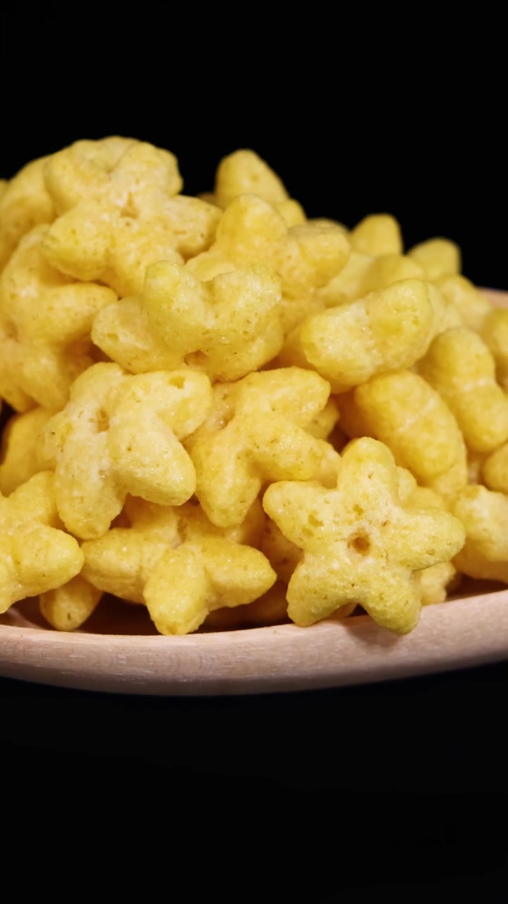 Cereali a forma di stella cadono da un cucchiaio di legno su uno sfondo nero, creando una scena dinamica e giocosa