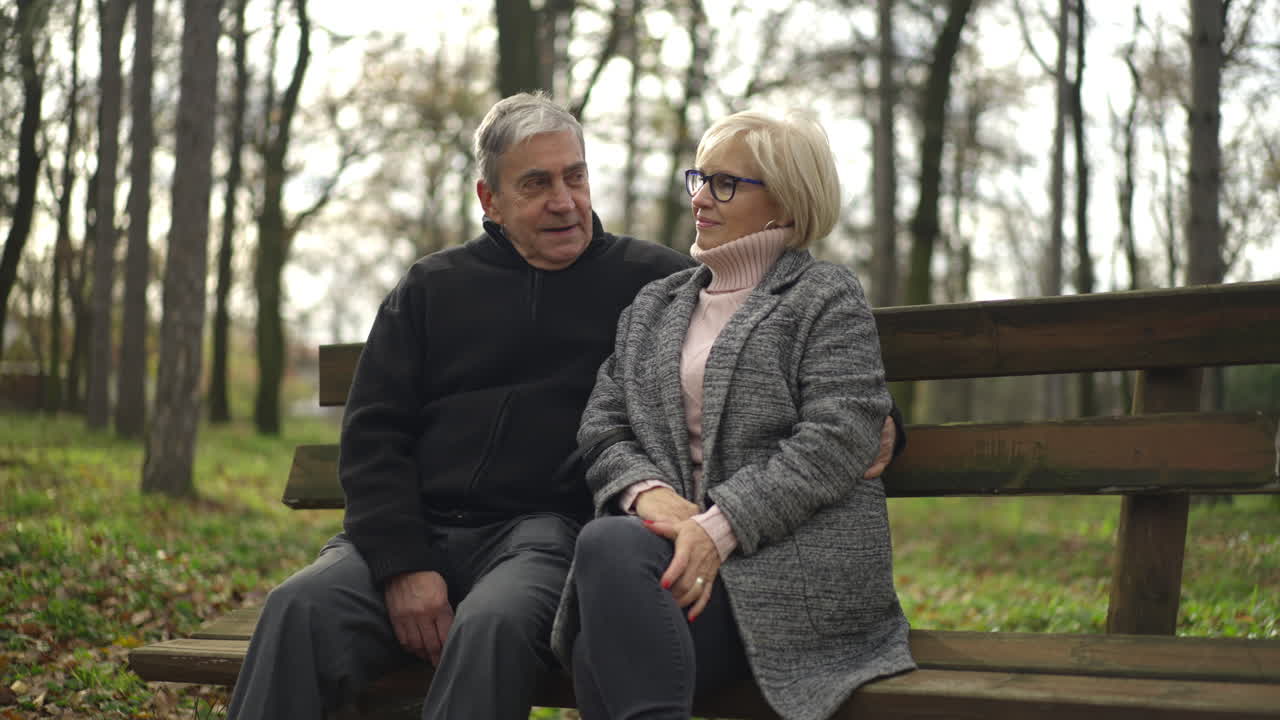 An elderly couple sitting on a bench in a park