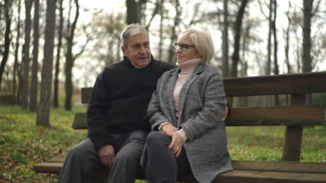 an elderly couple sitting on a bench in a park