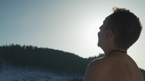 Close up view behind man breathing heavily while sitting outside in cold mountain environment with no shirt
