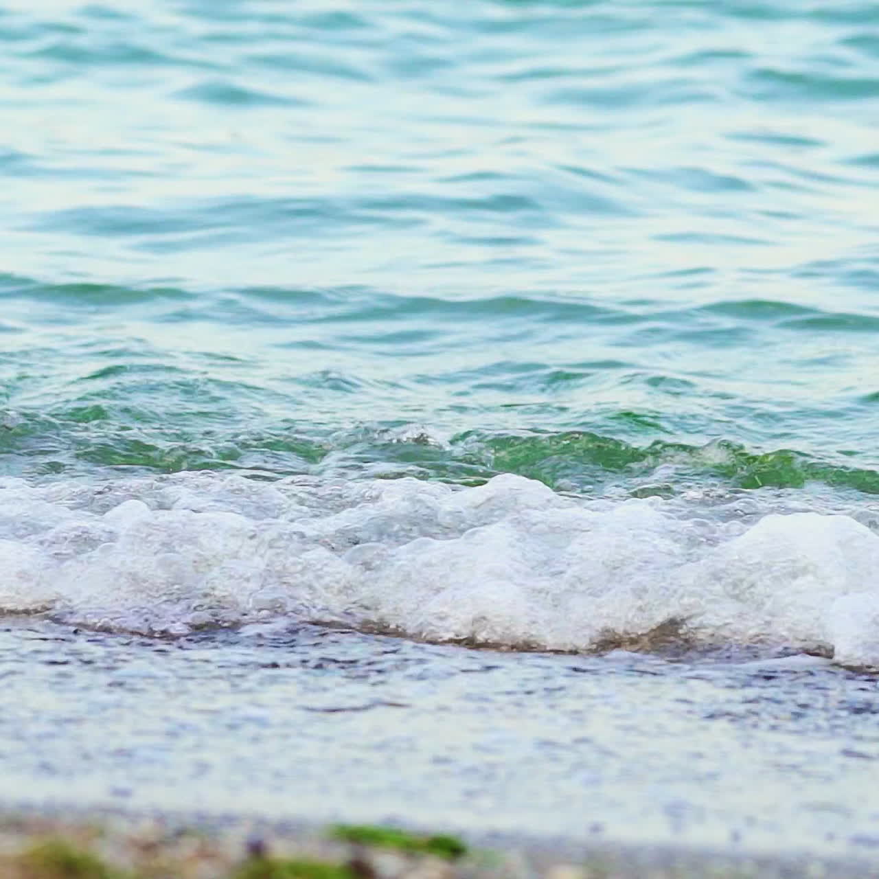 Water's waves dancing at the edge of the sea on a beach. White waves of transparent water on paradise beach in summer. Slow motion. Cose-up