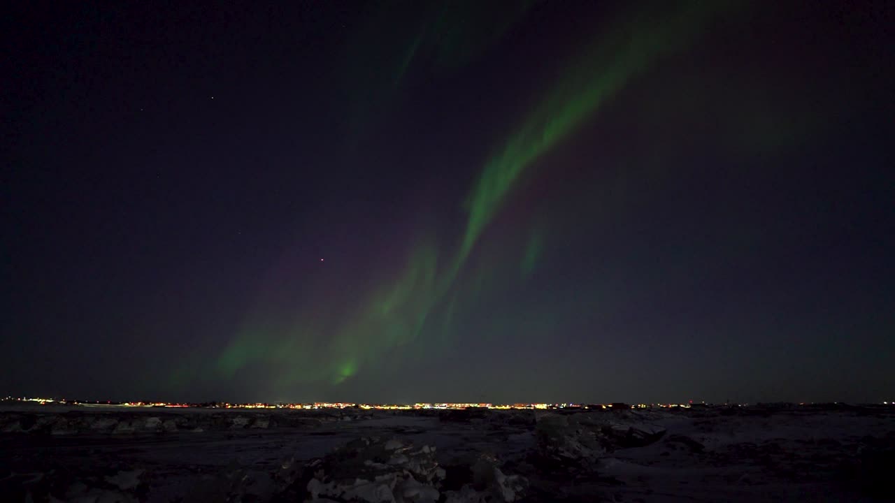 Flashing lights at night sky over icelandic city. Warm lighting cityscape with lantern and streetlights. Time lapse wide shot.