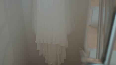 layered white wedding dress hangs indoors, creating a soft and serene atmosphere before the ceremony