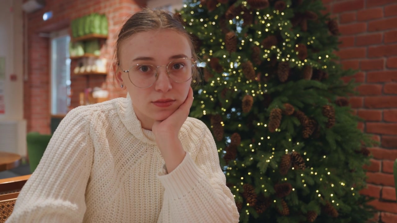 Thoughtful Young Woman Writing and Looking at Camera in Festive Cafe