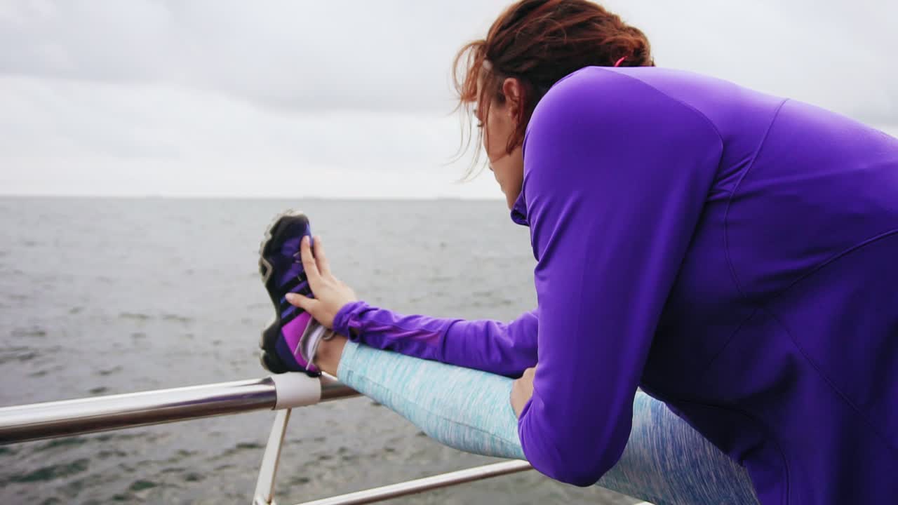 vista de fondo de una mujer joven estirando las piernas antes de correr en la playa junto al mar temprano en la mañana.