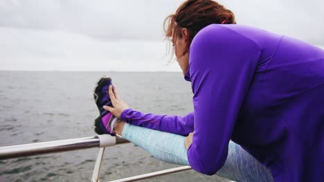 Vista-Posterior-De-Cerca-De-Una-Mujer-Joven-Estirando-Las-Piernas-Antes-De-Correr-En-La-Playa-Junto-Al-Mar-Temprano-En-La-Mañana.-Entrenamiento-Por