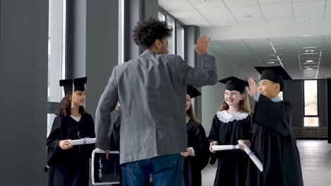 Group-Of-Happy--Preschool-Students-In-Mortarboard-And-Gown-Greeting-Their-Teacher