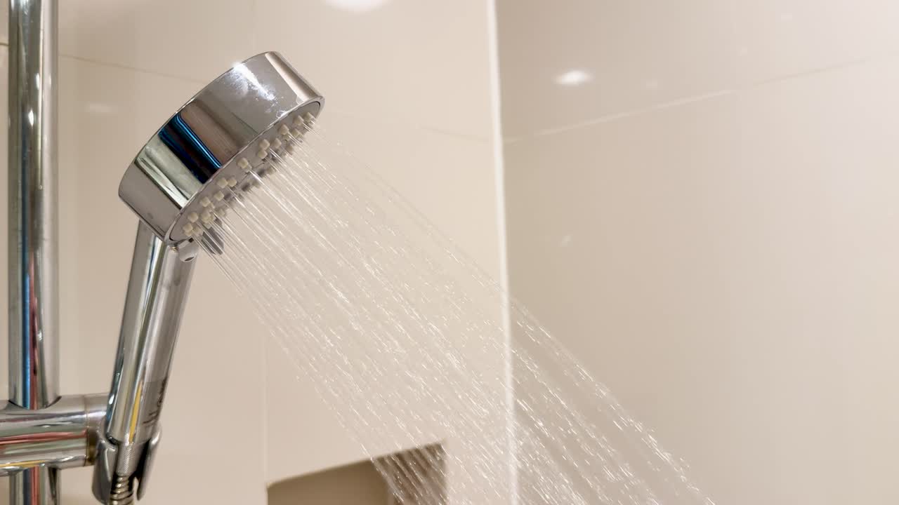 Water streams from chrome shower head in bright bathroom, captured in slow motion, steady shot