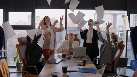 un grupo de felices compañeras de negocios en trajes de negocios arrojan hojas de papel en nombre de su victoria y éxito mientras trabajan en la oficina en la mesa